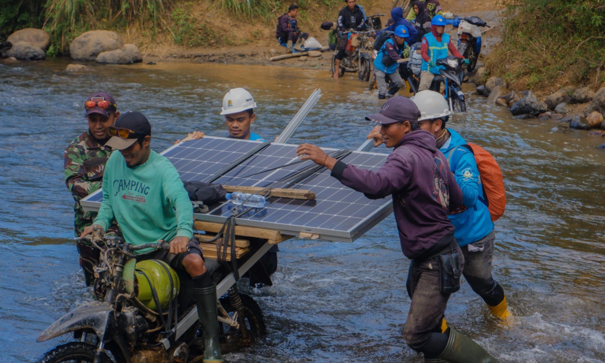 Petugas PLN dan warga Seko membawa panel surya melintasi sungai dalam Program Listrik Desa SuperSUN.
